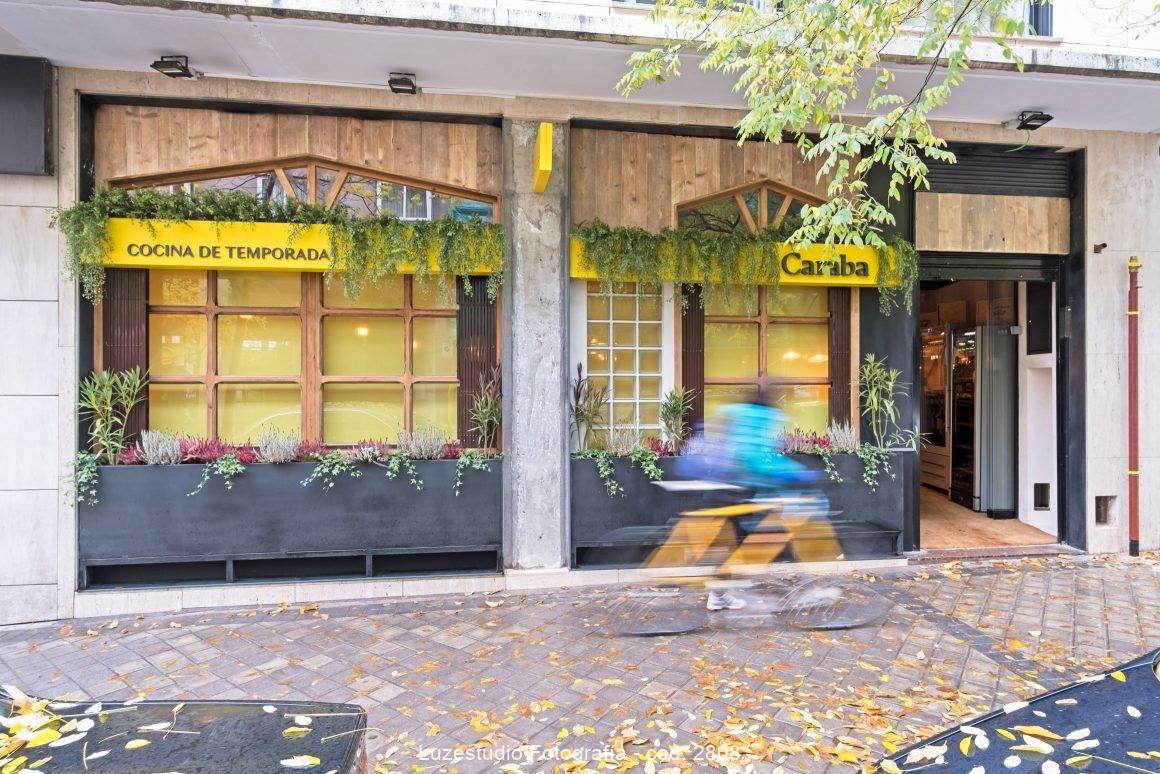 fachada de restaurante en otoño con hojas amarillas y una persona con abrido azul pasando con la bicicleta