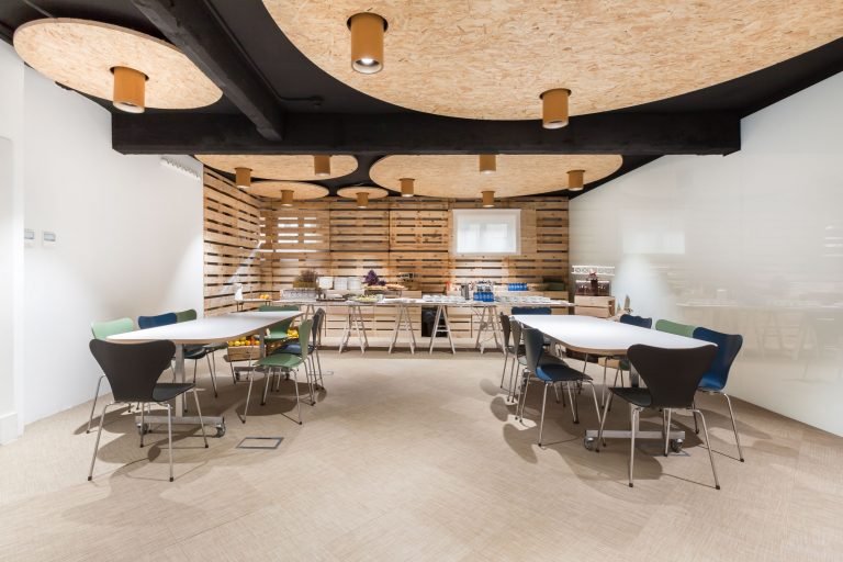 espacio central IE Student hub con mesas de trabajo y bufét de desayuno al fondo