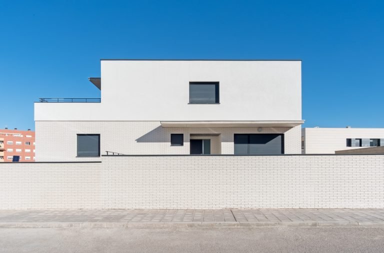 fachada calle de una casa con ventanas cerradas pared blanca y muro de ladrillo crema en guadalajara fotografo de arquitectura