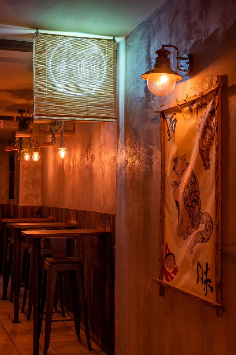 entrada de restaurante japonés con cuadro de tela y mesasa altas