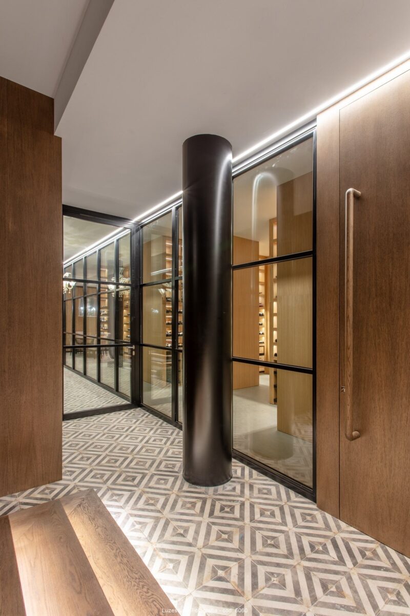 hall con columna negra escaleras iluminadas con led suelo hidraulico y puerta de madera en bodega