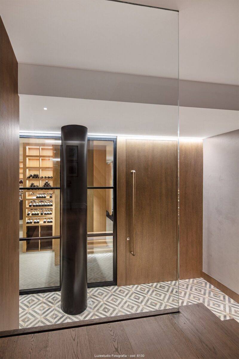 separador de cristal en bajada por escalera de madera hacia entrada a bodega privada en chalet de madrid