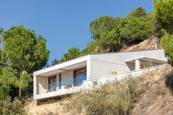 vivienda modular de hormigón cn balcón rodeada de pinos en terreno con 20 metros de desnivel