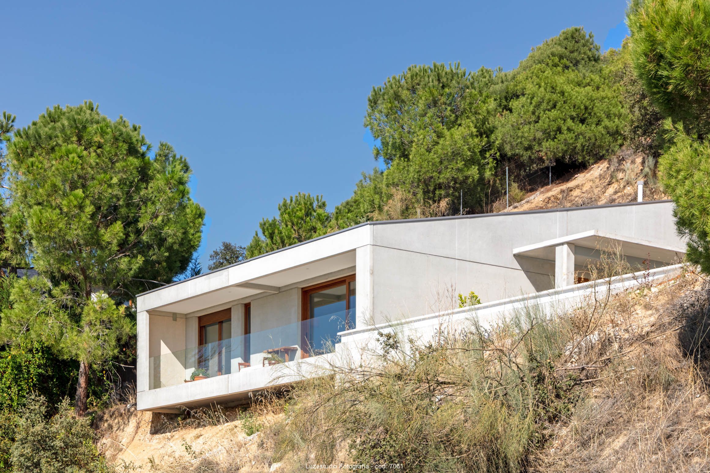 vivienda modular de hormigón cn balcón rodeada de pinos en terreno con 20 metros de desnivel
