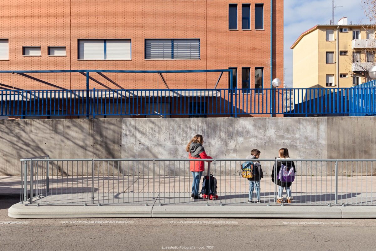dos niñas y un niño con mochilas en plataforma de cemento ampliacion de acera frente a una escuela de madrid