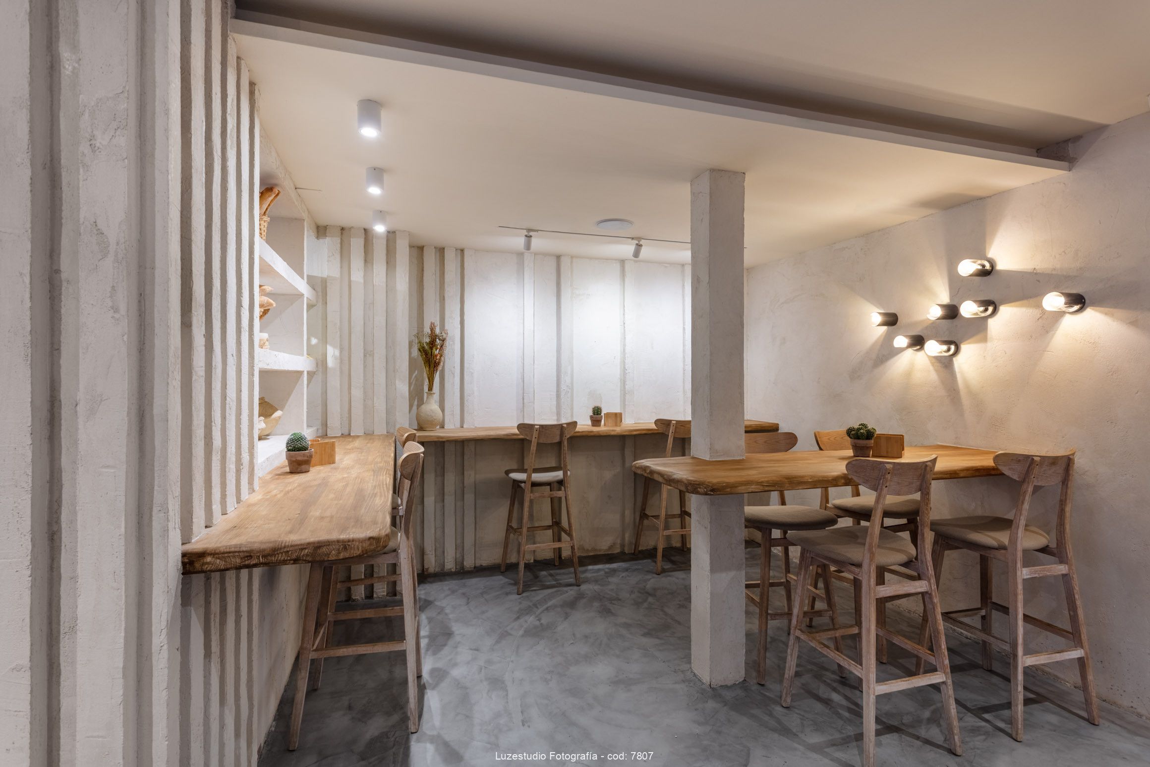 Fotógrafa de interiores alina banta reportaje interiorismo para francisco segarra (1) fotografía interior de cafetería con pared de microcemento y mesas de madera con sillas altas decoradas con cactus y luces puntuales