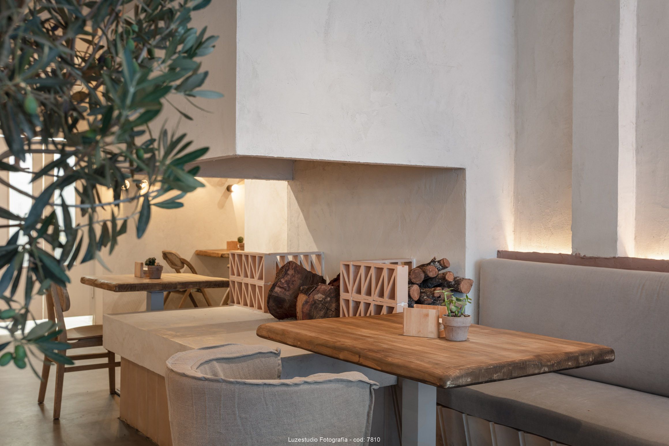 Fotógrafa de interiores alina banta reportaje interiorismo para francisco segarra (4) mesa de madera en interior de cafetería con chimenea de cemento pulido, troncos de madera y ojas de olivo