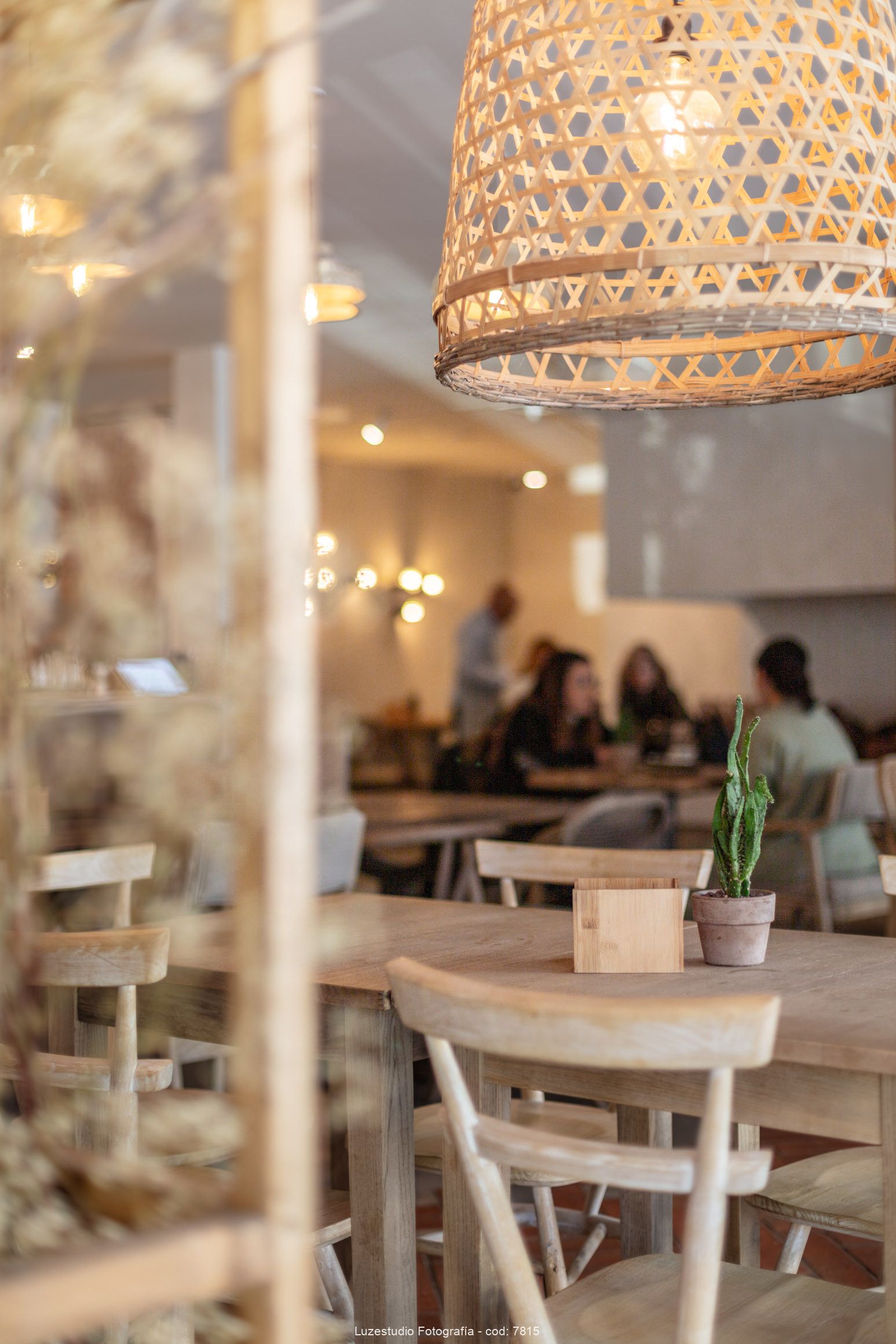 lampara de mimbre mesa y sillas de madera en cafeteria con gente desenfocada al fondo