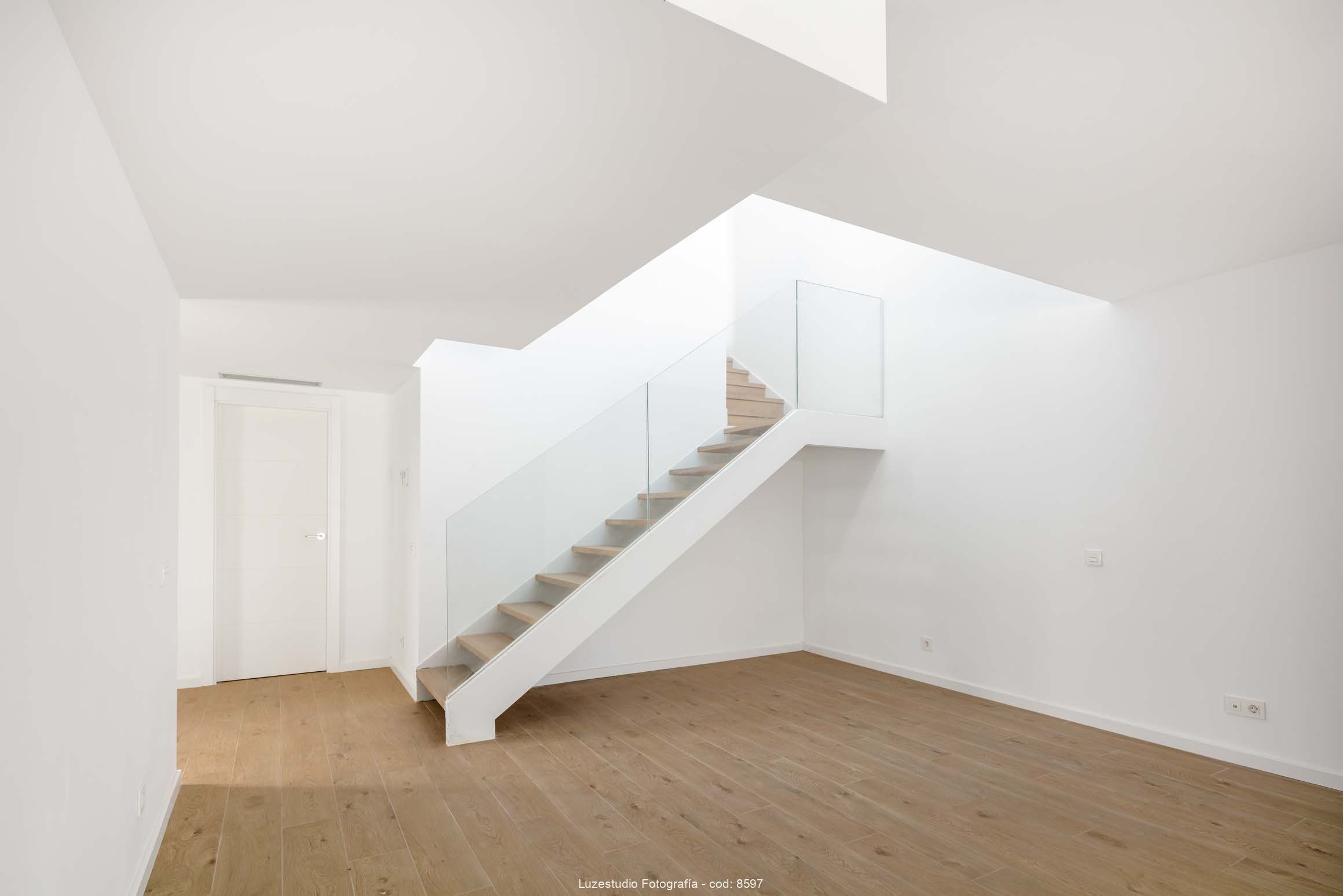 sala de estar vacia con paredes blancas, parquet y escalera de madera con cristal