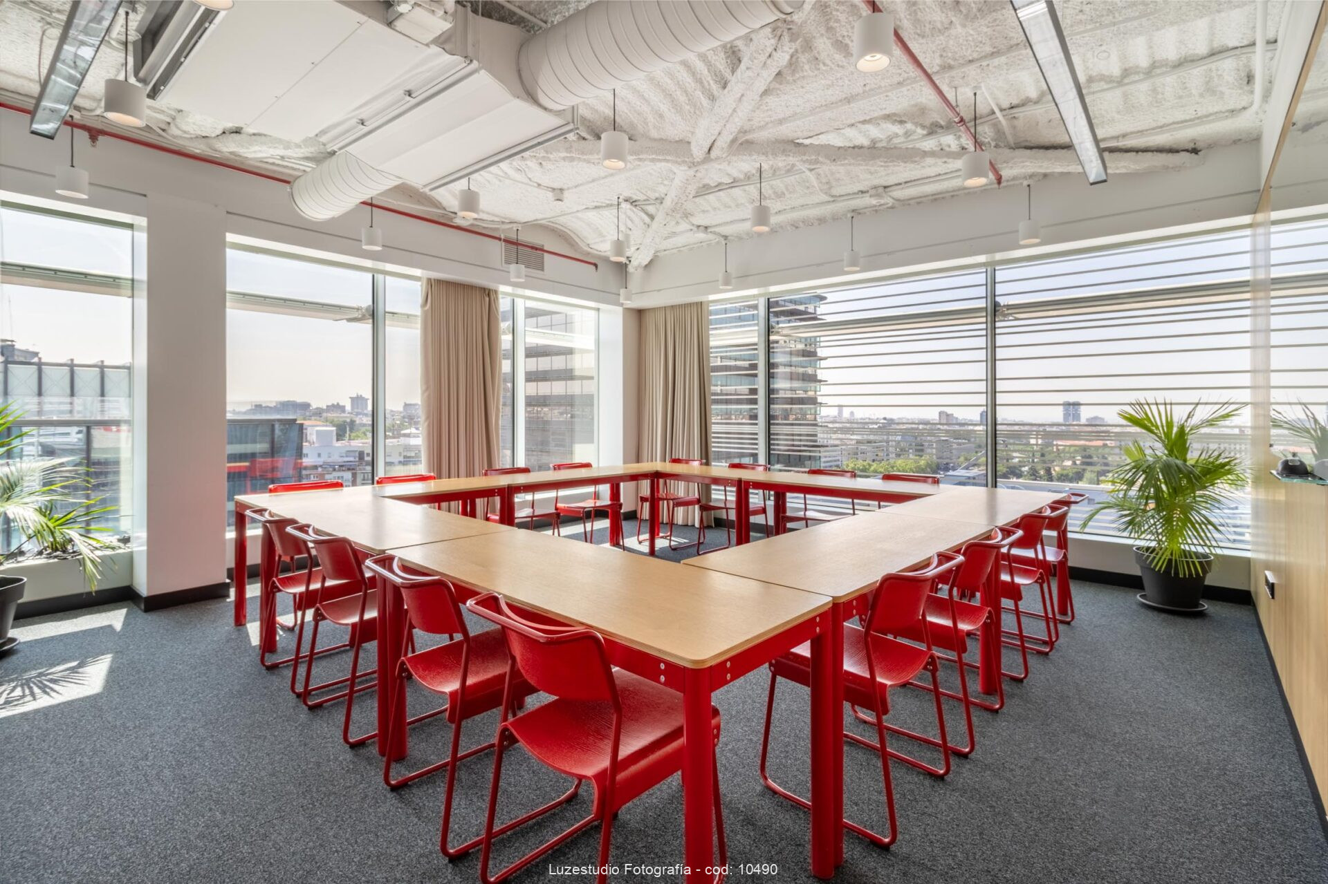 mesas de madera con perfileria metálica roja y sillas rojas en sala de reuniones con vistas sobre madrid y techo técnico