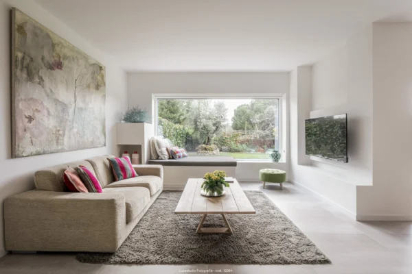 Salón luminoso con sofá crema, gran cuadro colgado, cojines de colores y jardín al fondo